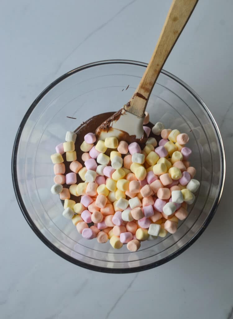 Overhead view of mini marshmallows in a bowl of melted chocolate and peanut butter.