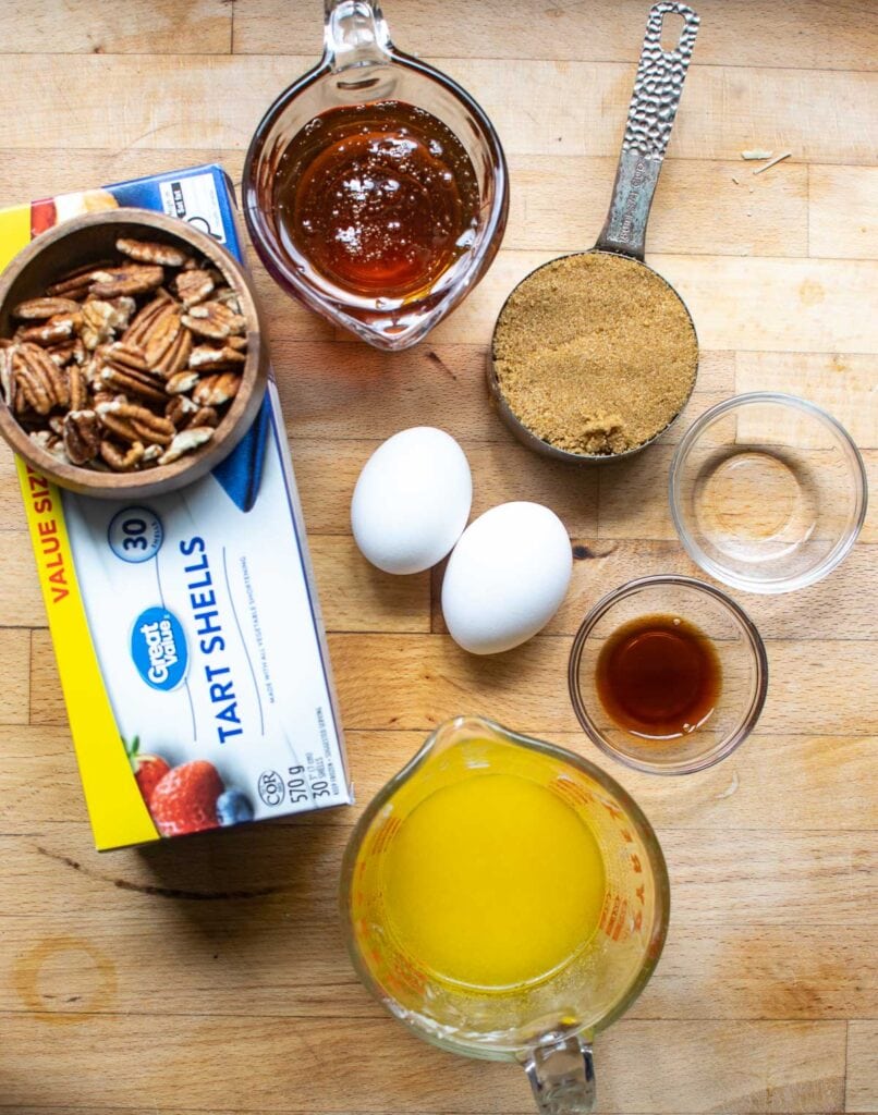 Ingredients to make pecan butter tarts including pre-made tart shells, brown sugar, corn syrup, eggs and melted butter.