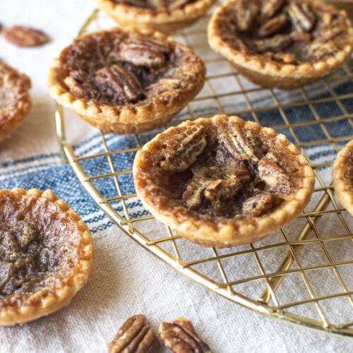 A gold cooling rack with 3 pecan butter tarts and one plain butter tart.