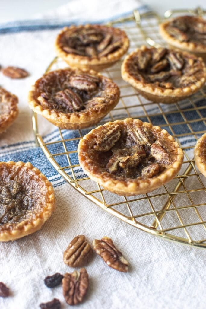 A gold cooling rack with 3 pecan butter tarts and one plain butter tart.