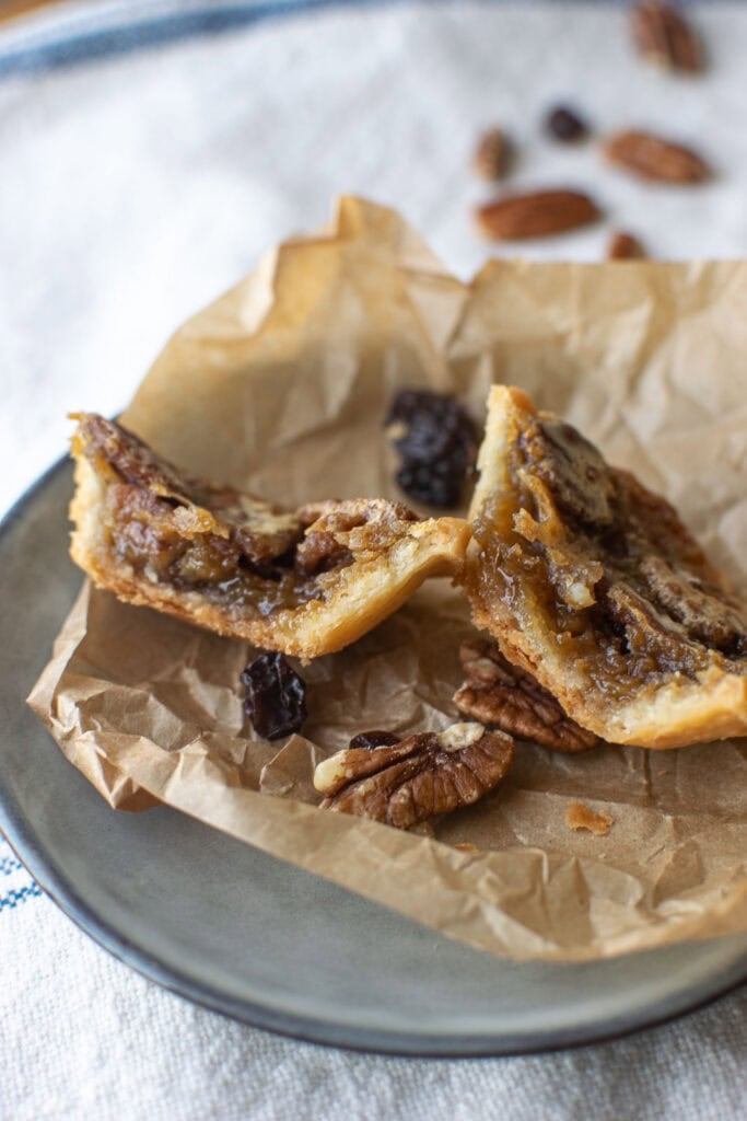 Pecan butter tarts cut in half to show the filling on top of crumbled parchment paper.