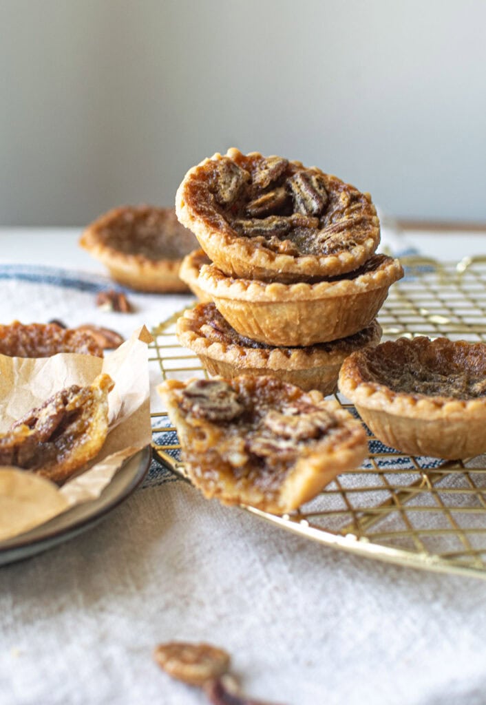 A stack of pecan butter tarts on a gold cooling rack with one cut in half in front of the stack.