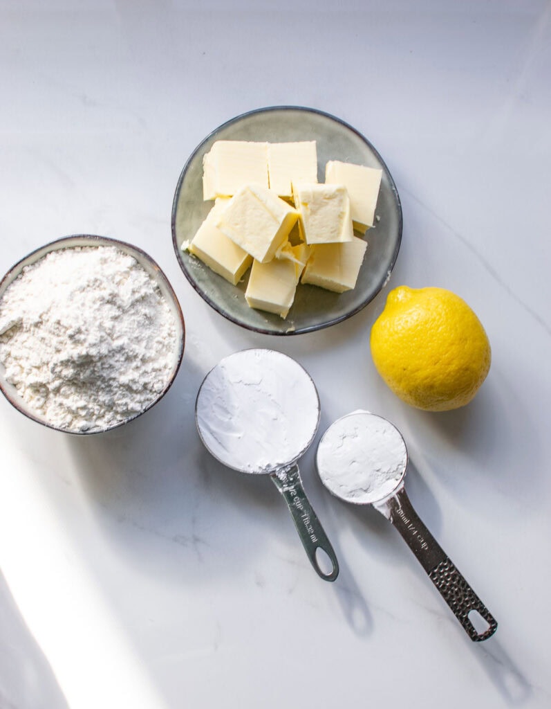 Ingredients to make lemon shortbread snowball cookies including flour, icing sugar, cornstarch, butter and a lemon.