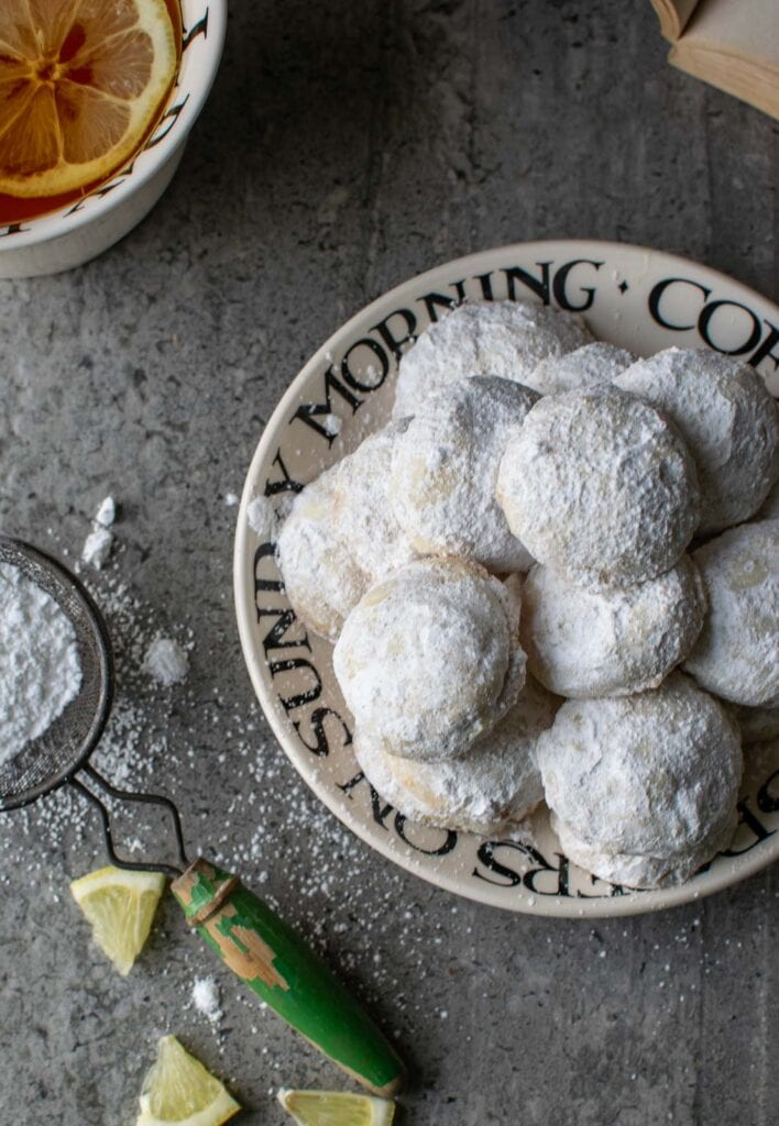A plate of lemon snowball cookies thoroughly coated with powdered sugar.