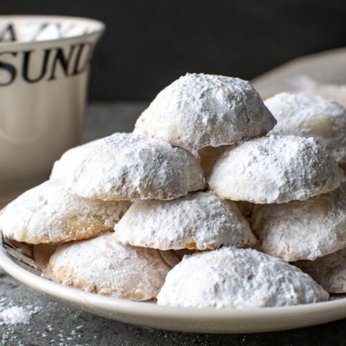 A plate of lemon shortbread snowball cookies with a teacup beside the plate.