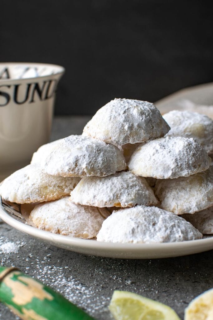 A plate of lemon shortbread snowball cookies with a teacup beside the plate.