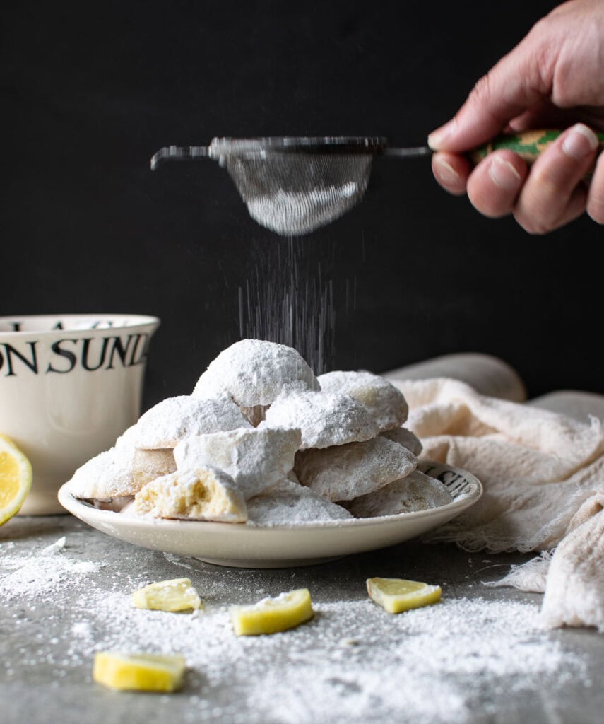 Powdered sugar being sifted onto lemon shortbread ball cookies.