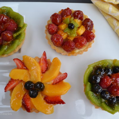 Four custard tarts decorated with fresh summer fruit.