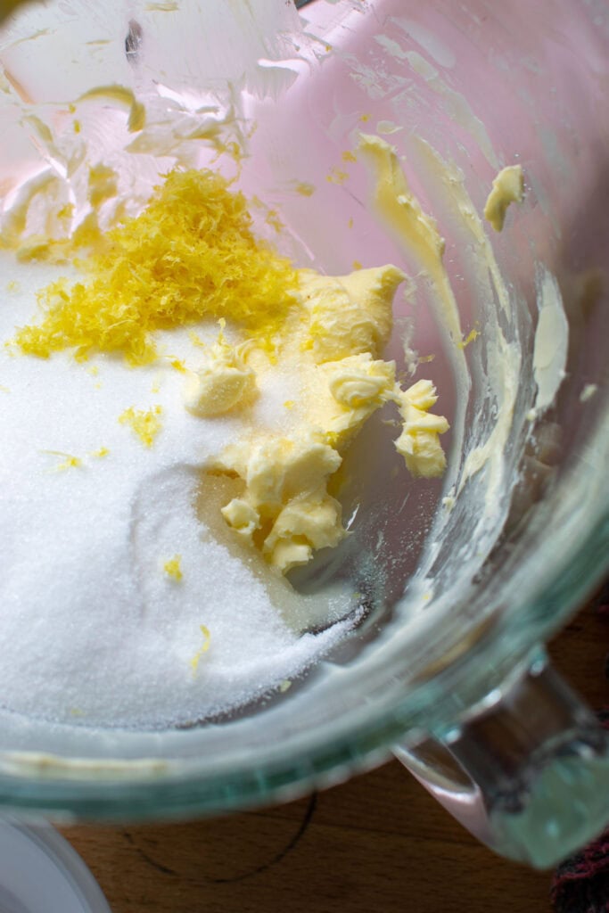 Sugar, lemon peel, and lemon zest added to the beaten butter in bowl of stand mixer.