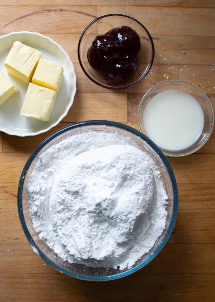 Ingredients to make raspberry frosting including icing sugar, butter, milk and raspberry jam.