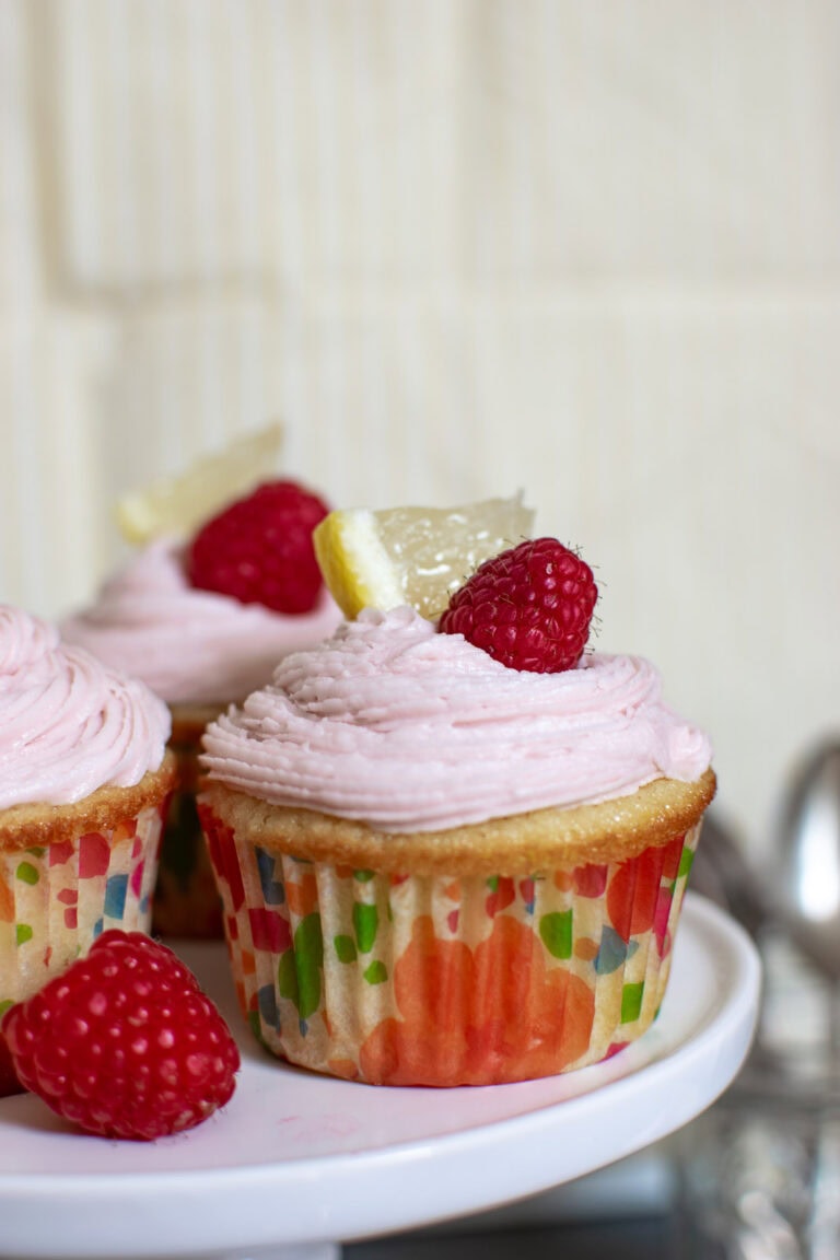 Pink Lemonade Cupcakes garnished with a lemon slice and fresh raspberry.