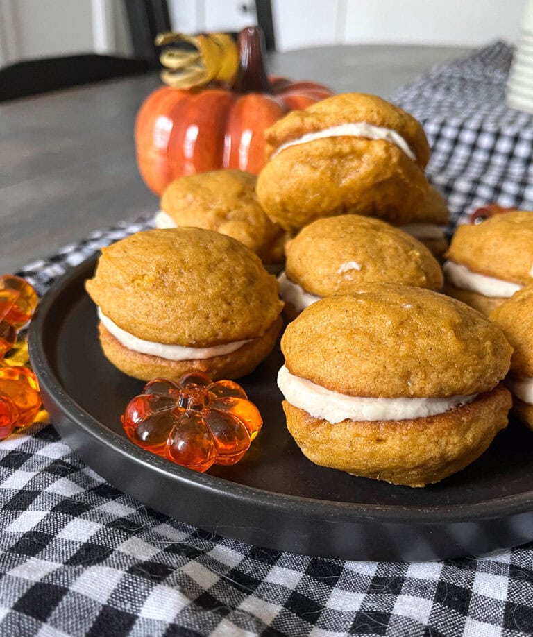 A tray of mini pumpkin whoopie pies with cream cheese filling on a black and white gingham tea towel.