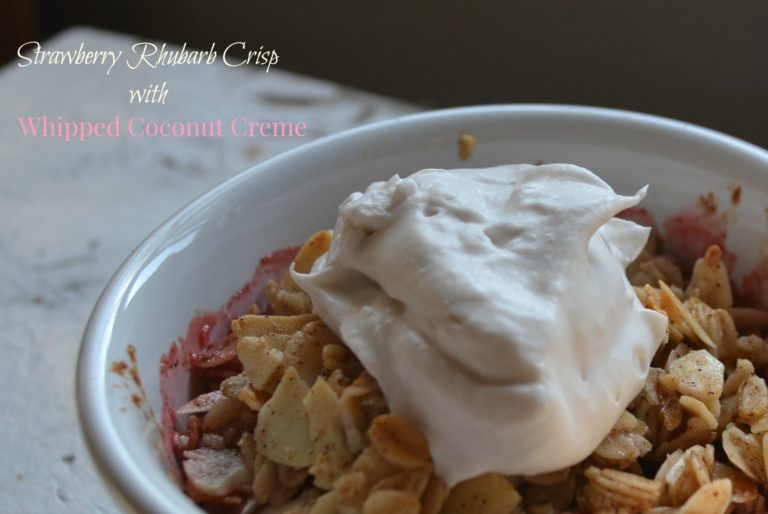 Strawberry rhubarb crisp in a white ramekin stopped with whipped cream.