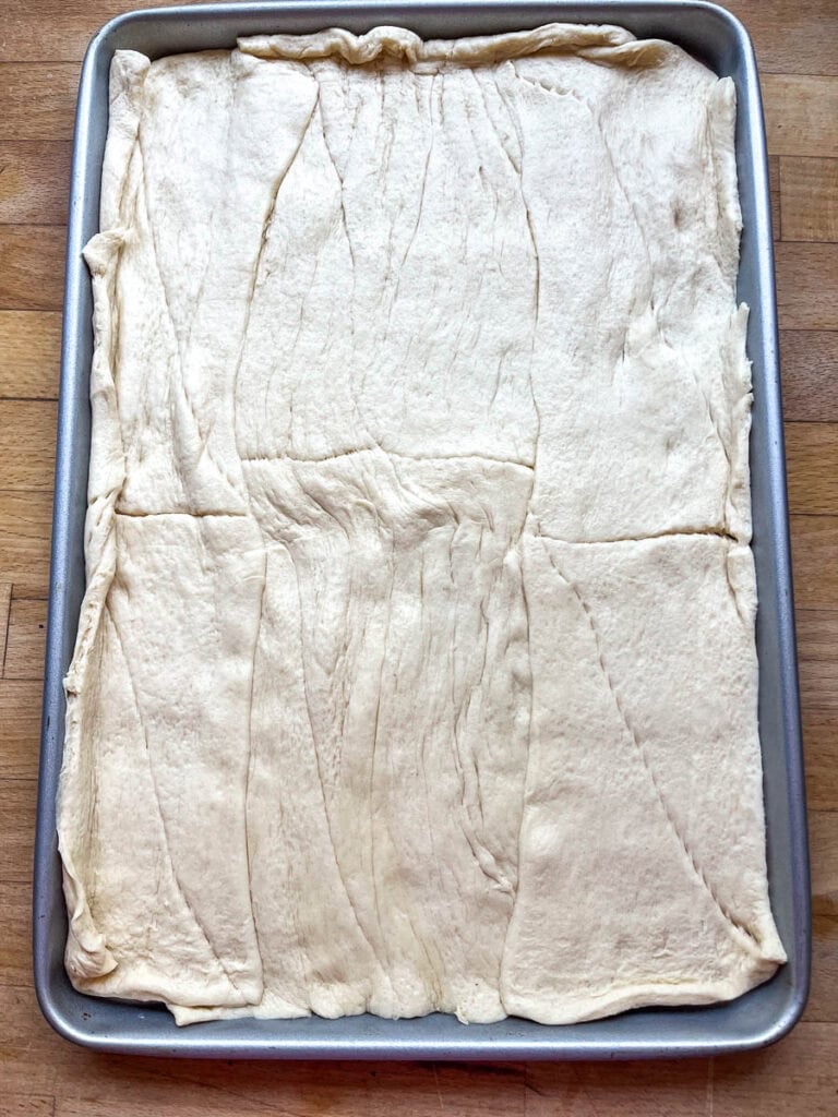 Crescent rolls rolled out to fit a rimmed baking sheet before baking.