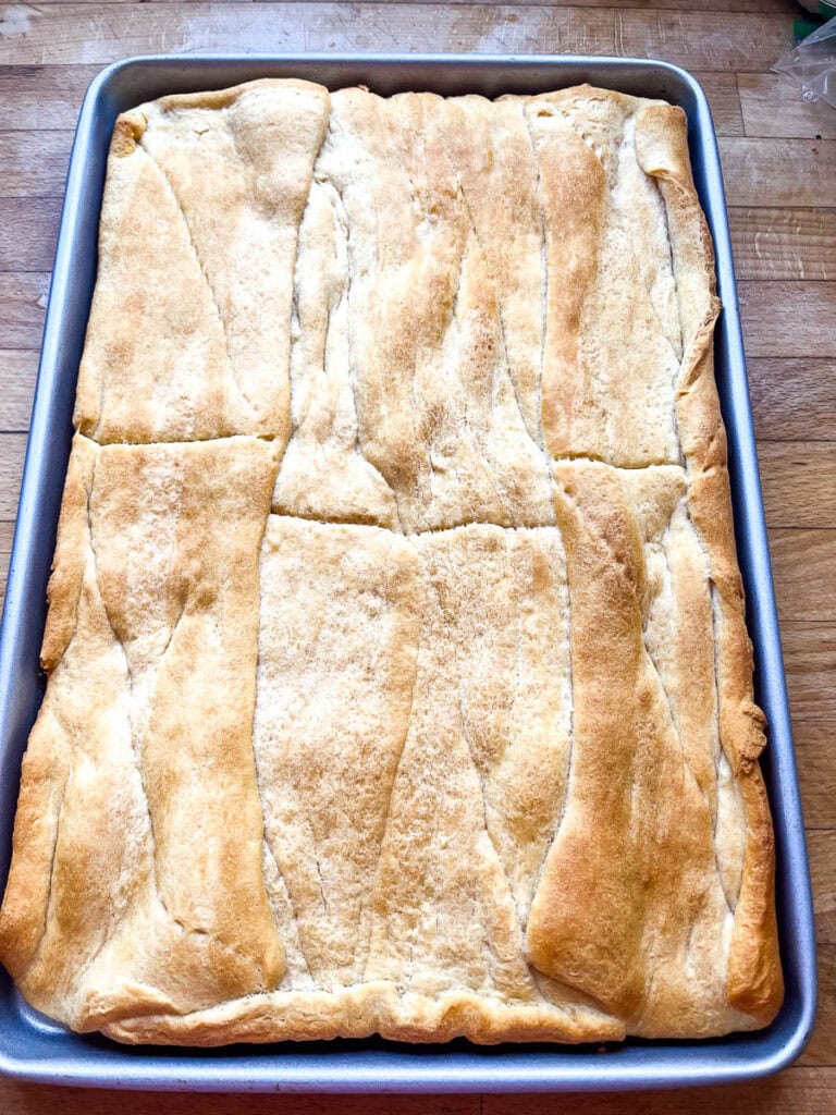 Freshly baked crescent rolls that have been rolled out to fit a rimmed cookie sheet.