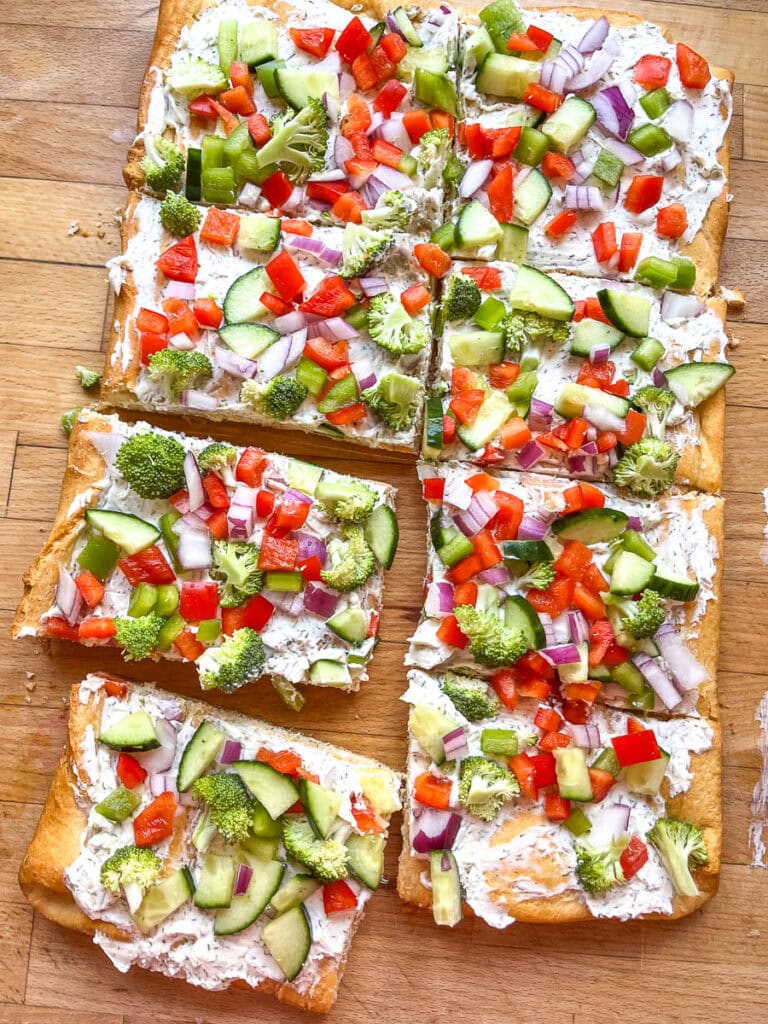 A rectangle shaped Crescent Roll Veggie Pizza cut into 8 large squares, topped with red pepper, broccoli, green pepper and red onion.
