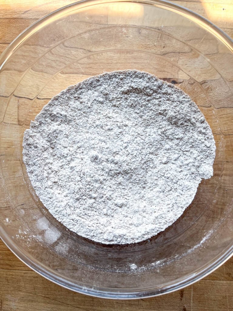 Dry ingredients including flour, baking powder, baking soda, brown sugar and pumpkin pie spice in a large glass mixing bowl.