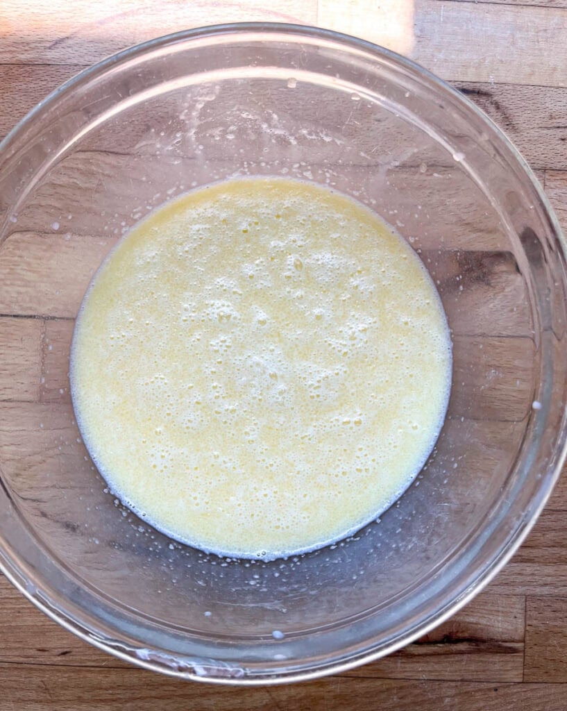 Wet ingredients to make pecan muffins including buttermilk, melted butter and eggs whisked together in a glass mixing bowl.