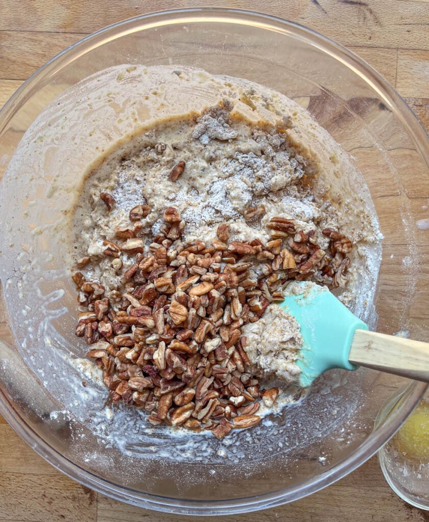 Wet and dry ingredients plus chopped pecans being stirred together in a large mixing bowl to make muffin batter.