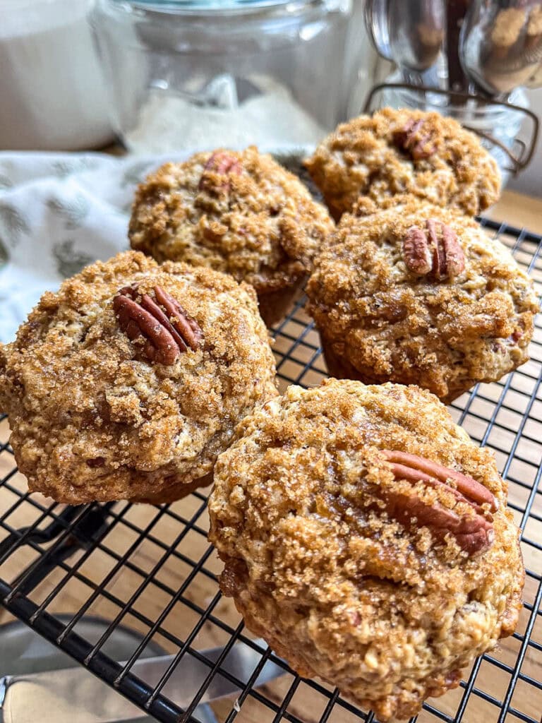 Butter Pecan muffins with a crumb topping and garnished with pecan half on a cooling rack.