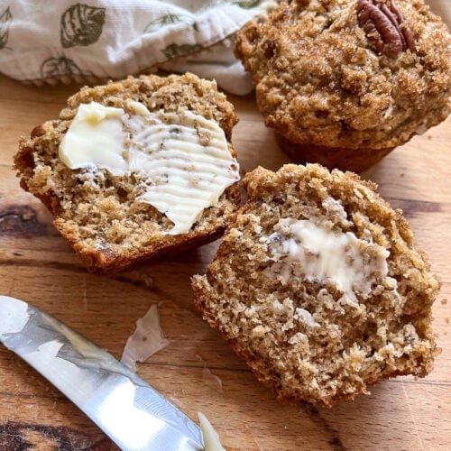 A whole butter pecan muffin in the background, and one cut in half and buttered in the foreground.