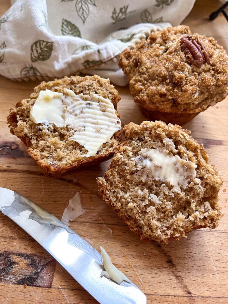 A whole butter pecan muffin in the background, and one cut in half and buttered in the foreground.