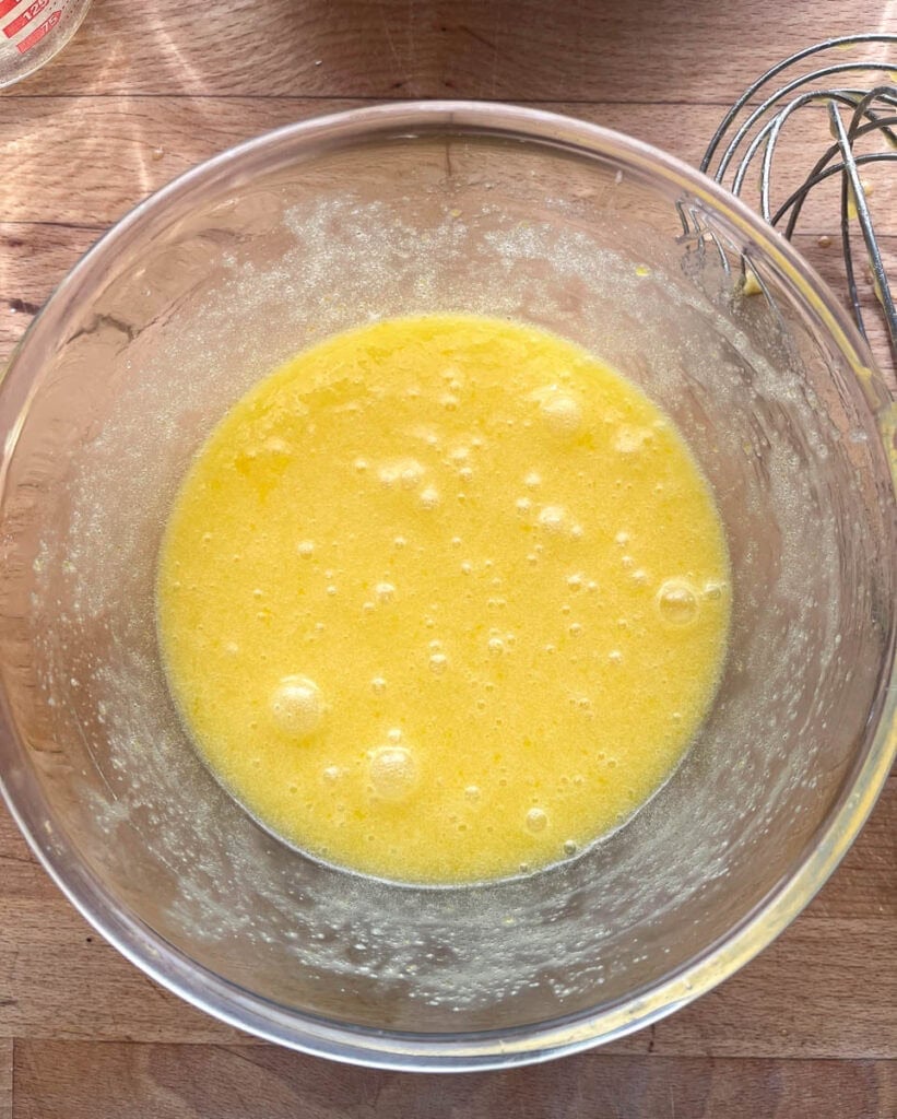 Eggs, sugar and melted butter whisked together in a large glass mixing bowl.