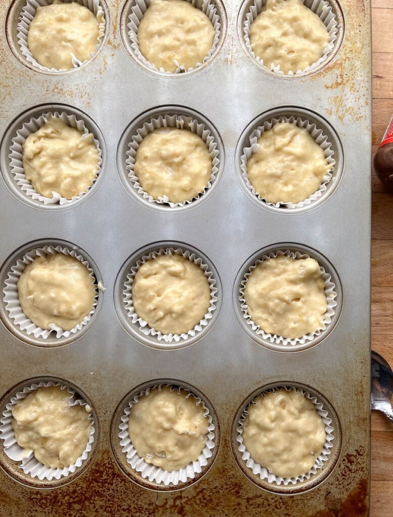 Banana muffin batter divided between 12 muffin tins before baking.