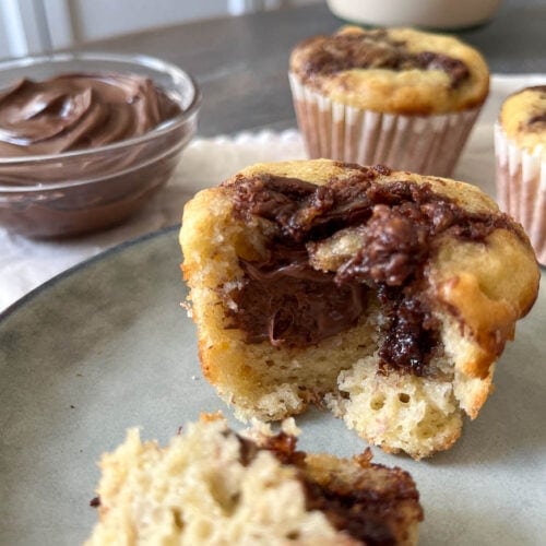 Banana Nutella Muffins, one cut in half to expose the middle, with a bowl of Nutella to the side.