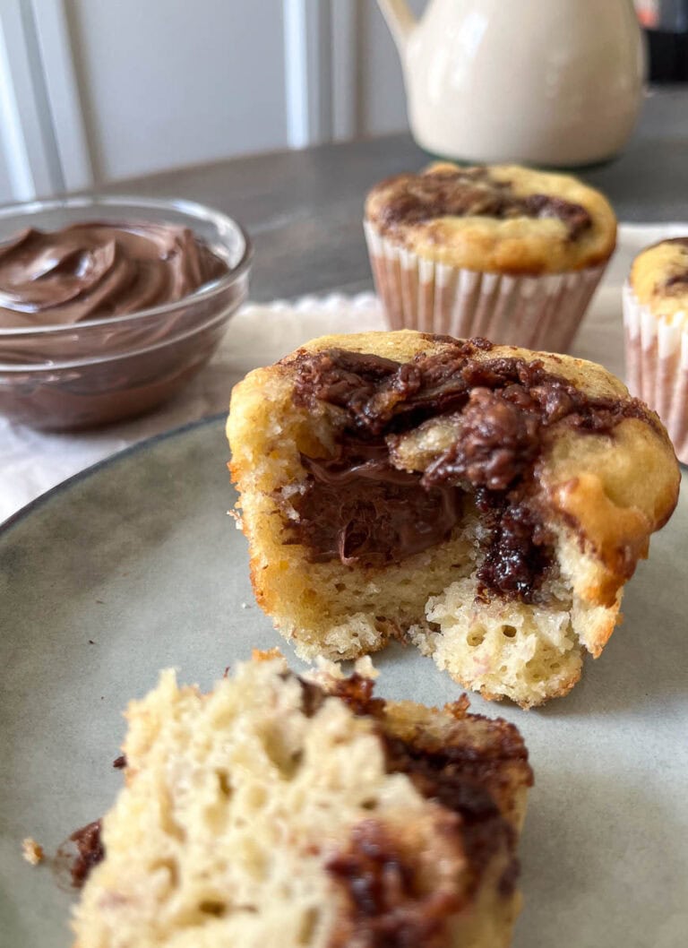 Banana Nutella Muffins, one cut in half to expose the middle, with a bowl of Nutella to the side.
