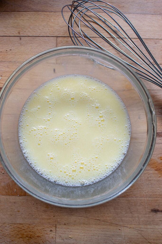 Liquid ingredients to make a cherry quick bread whisked in a glass mixing bowl.