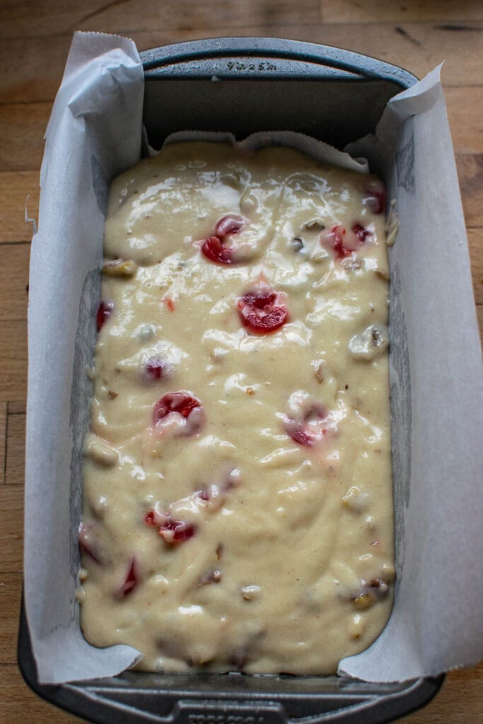 Cherry bread with walnuts in a loaf pan lined with parchment paper before baking.