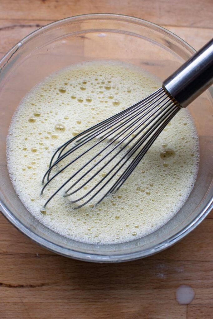Lavender infused milk, eggs and egg yolks beaten with a wire whisk in a mixing bowl.