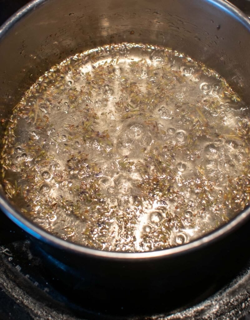 Lavender buds, sugar and water boiling in a pot on the stove top to make lavender simple syrup.