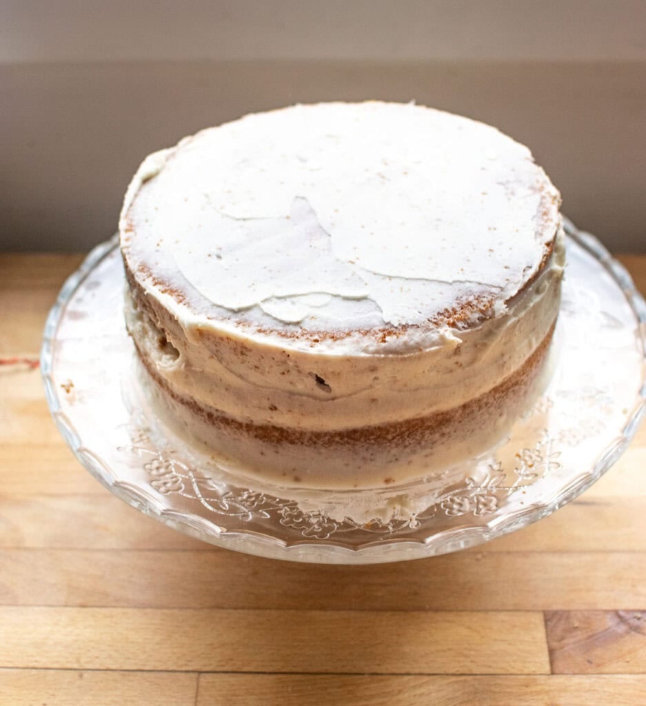 A Vanilla Lavender two layer cake on a cake stand with a crumb coat of frosting.
