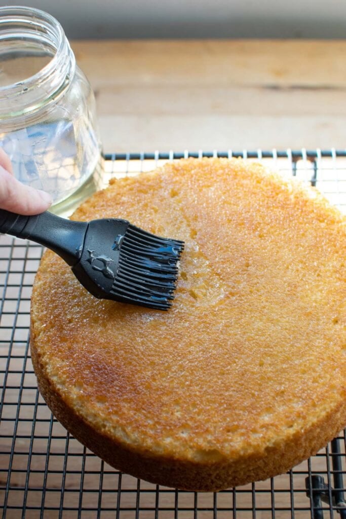 Freshly baked and cooled vanilla lavender cake being brushed with lavender simple syrup.