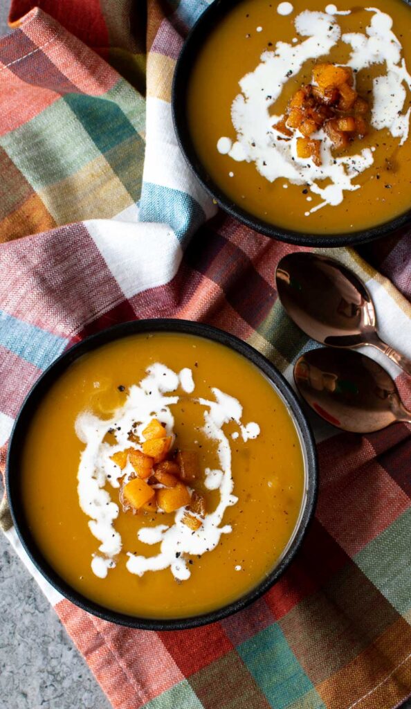 Two bowls of maple roasted butternut squash soup topped with fried butternut squash and cream.