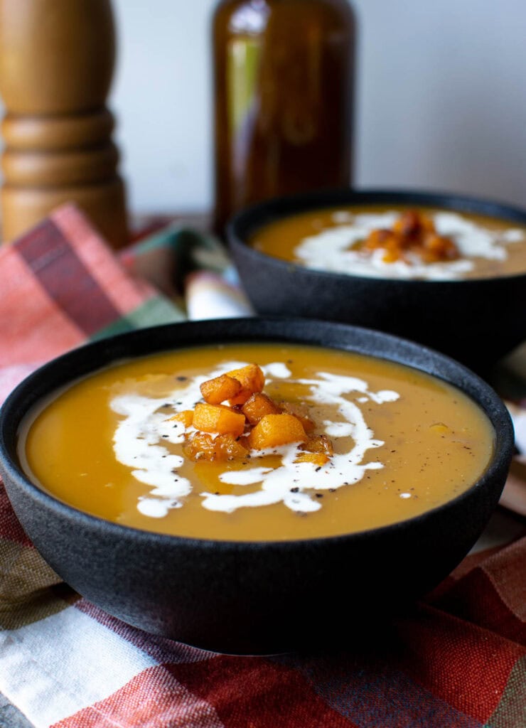 2 Bowls of Butternut squash soup garnished with a drizzle of cream and tiny pan fried pieces of squash.