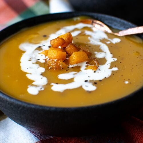 Bowl of butternut squash soup garnished with fried squash and drizzed with cream.