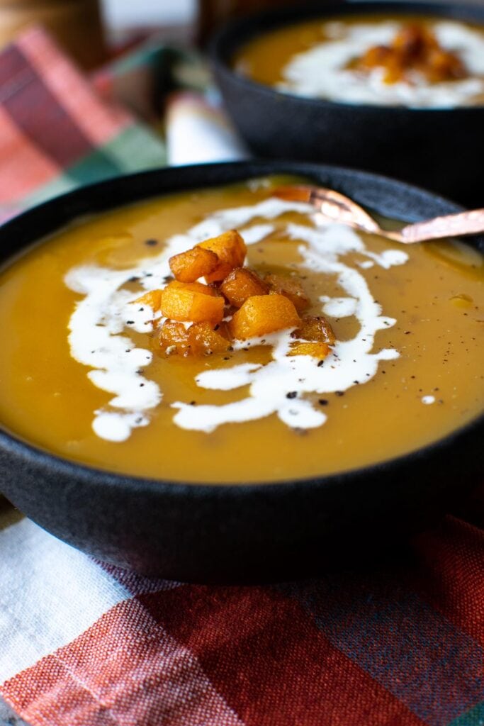 Bowl of butternut squash soup garnished with fried squash and drizzed with cream.
