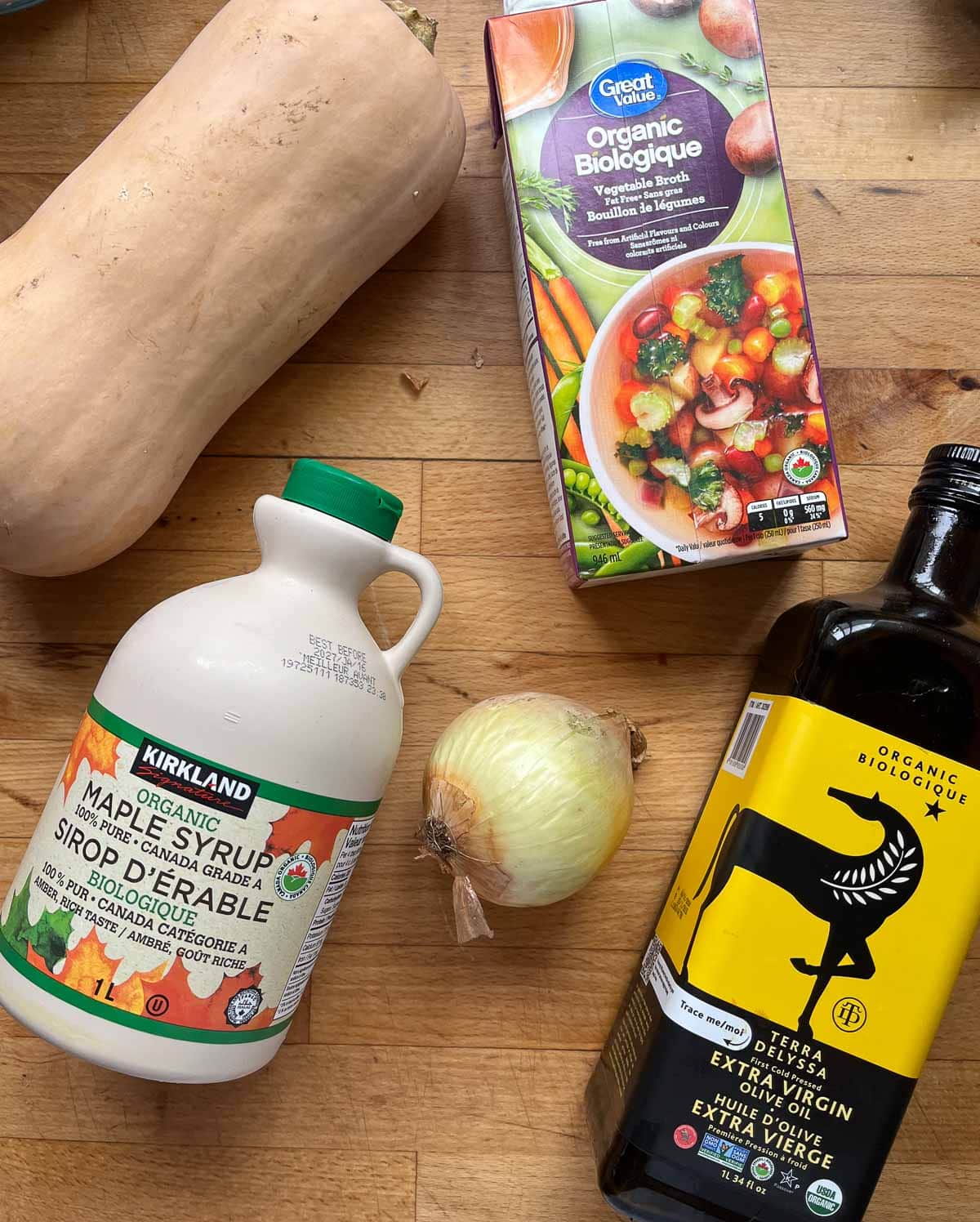 Ingredients to make maple butternut squash soup including olive oil, squash, maple syrup, onion and broth.