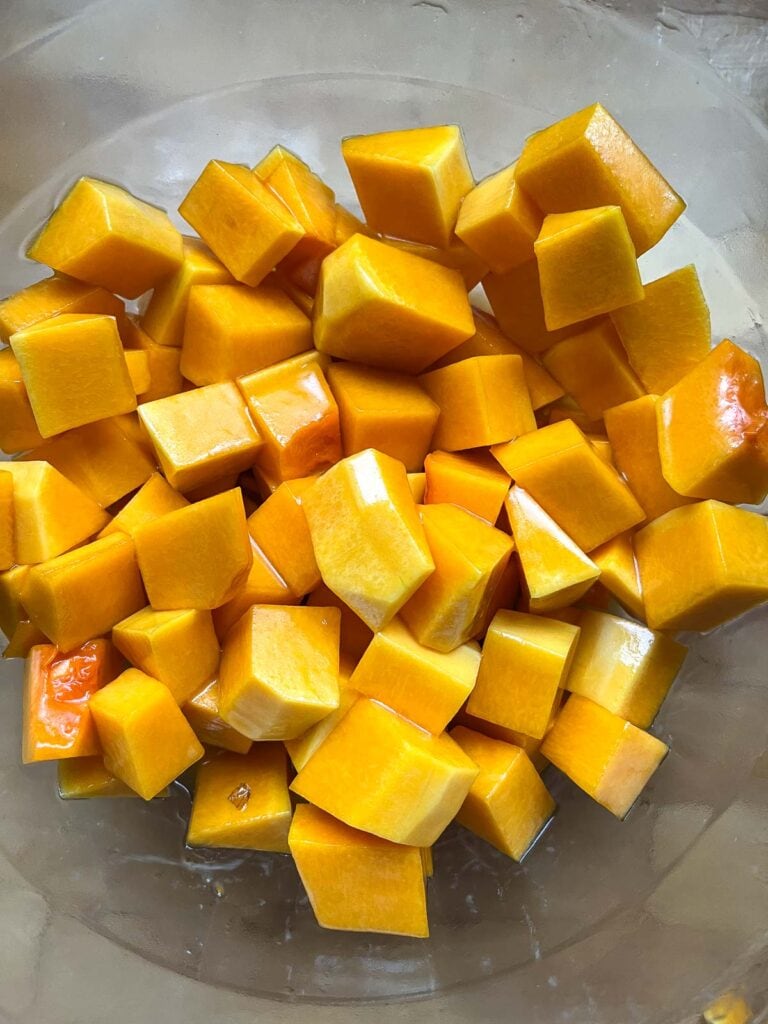 Cubed fresh butternut squash tossed with maple syrup and olive oil mixture in a mixing bowl.