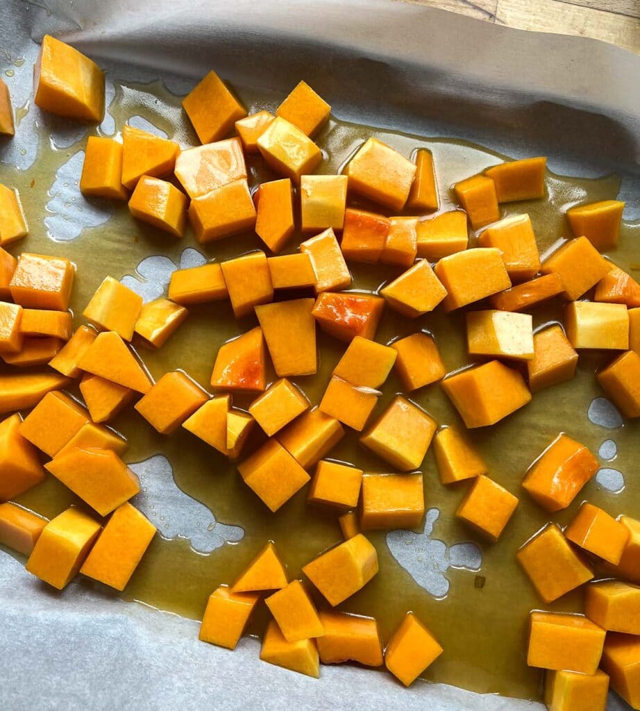 Butternut squash and maple syrup mixture on a parchment lined baking sheet before roasting.