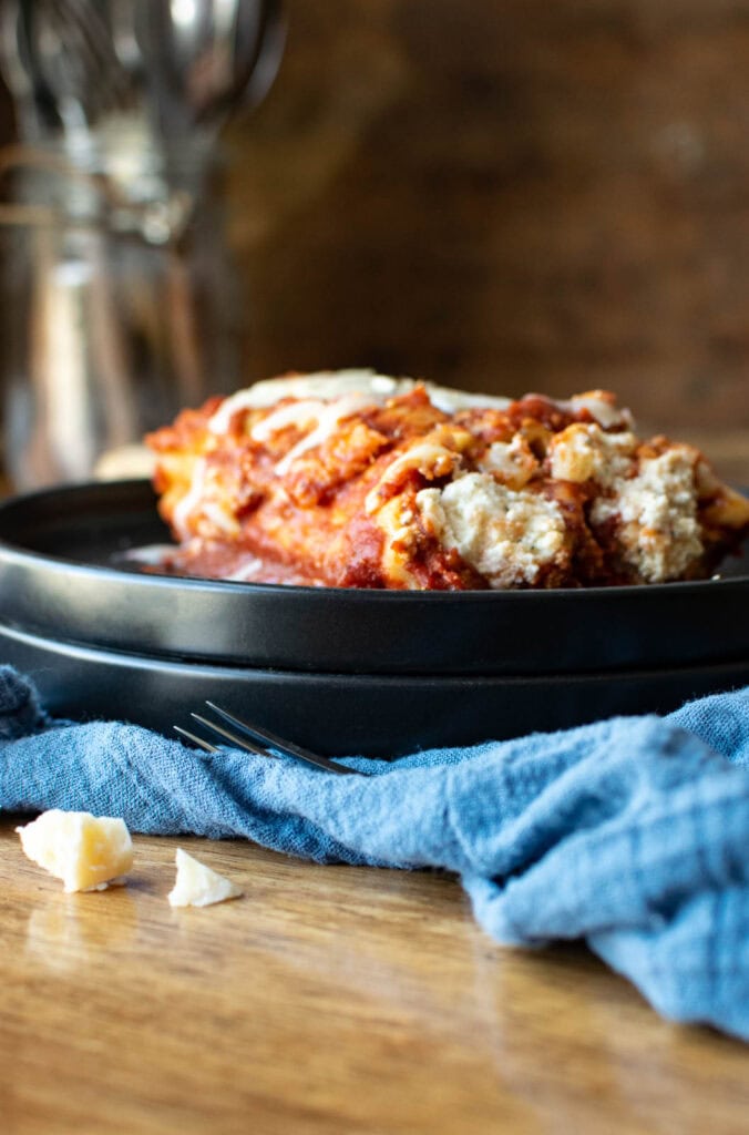 2 Manicotti noodles stuffed with 3 cheese mixture on a serving plate with a blue napkin underneath.