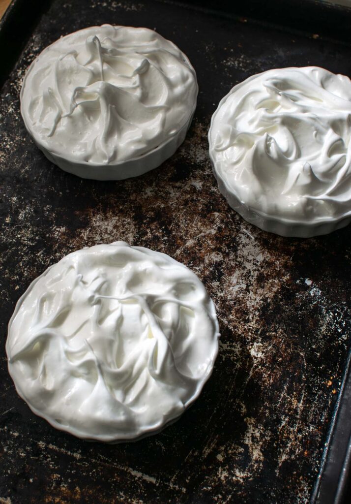 Fresh meringue spread and swirled on top of lemon pie filling in shallow ramekin dishes.