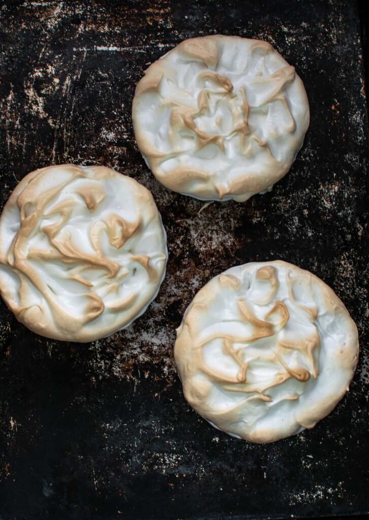 Lemon meringue tarts fresh out of the oven on a baking tray.