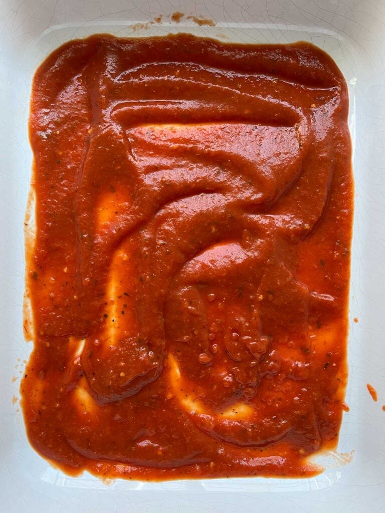 Marinara sauce spread over bottom of a casserole dish.