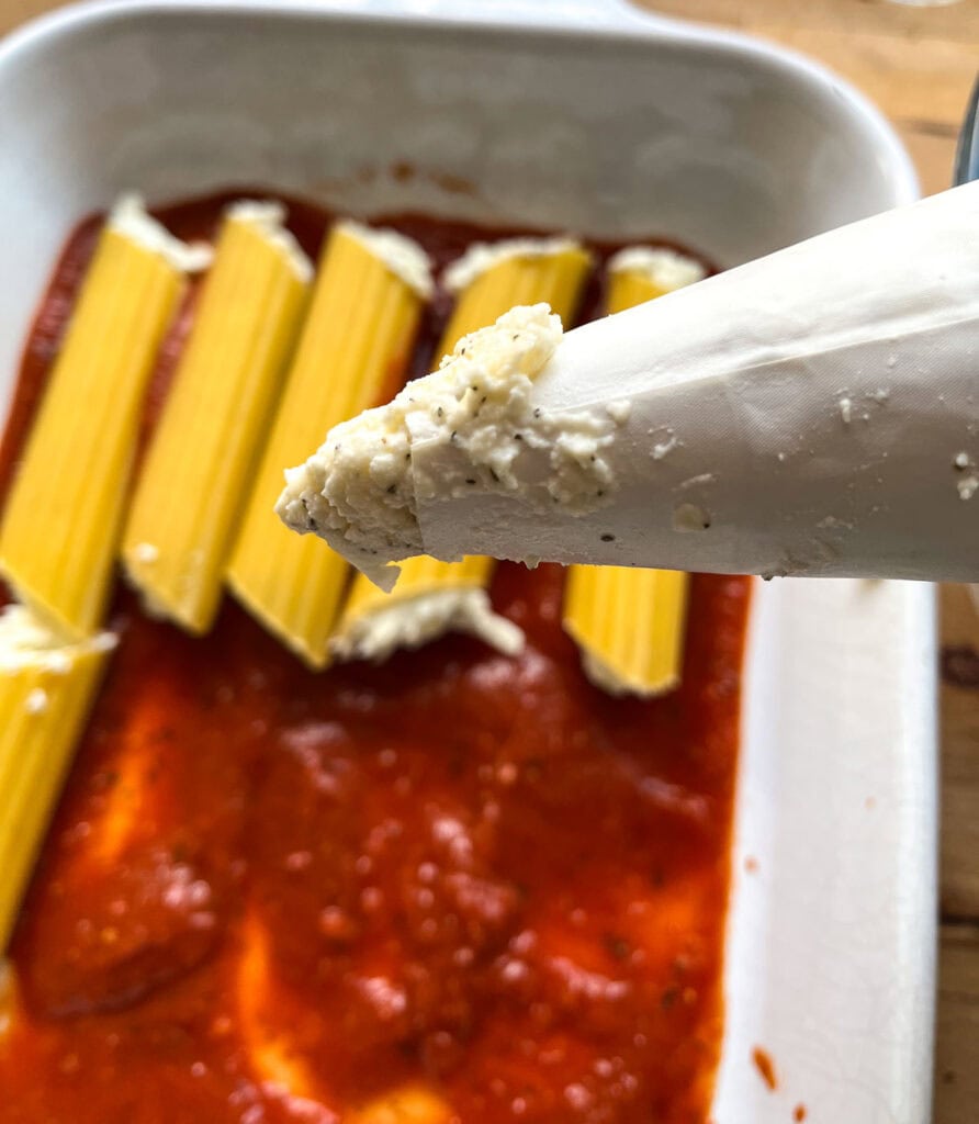 Dry manicotti shells being filled with cheese filling using a piping bag.