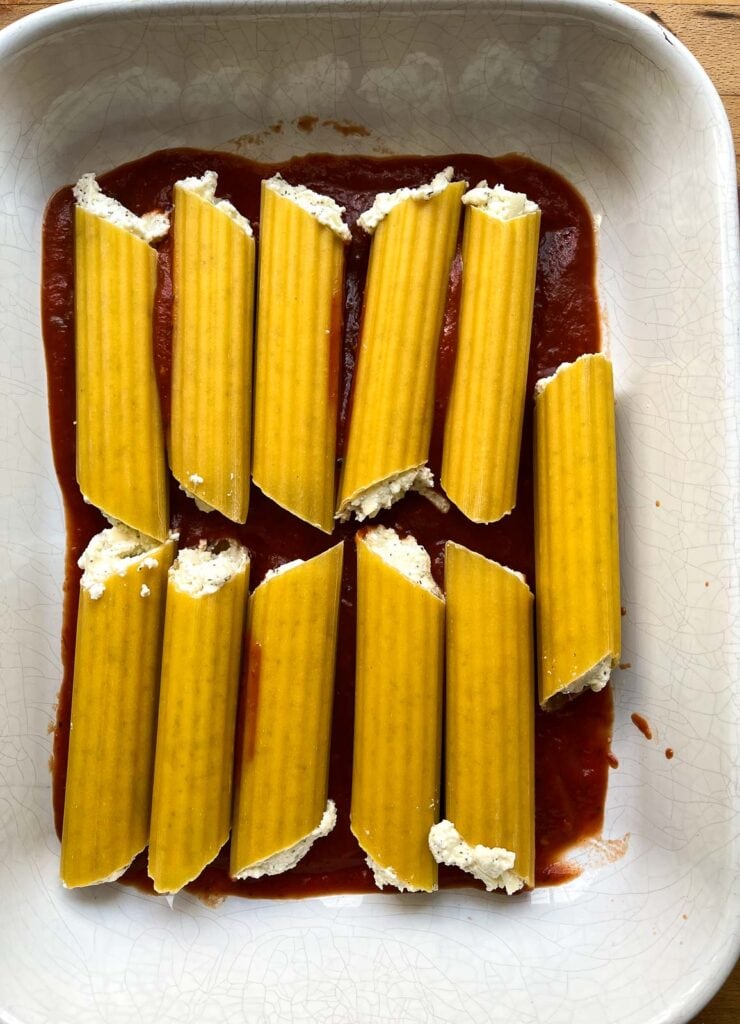 11 manicotti shells in a casserole dish on top of marinara sauce.