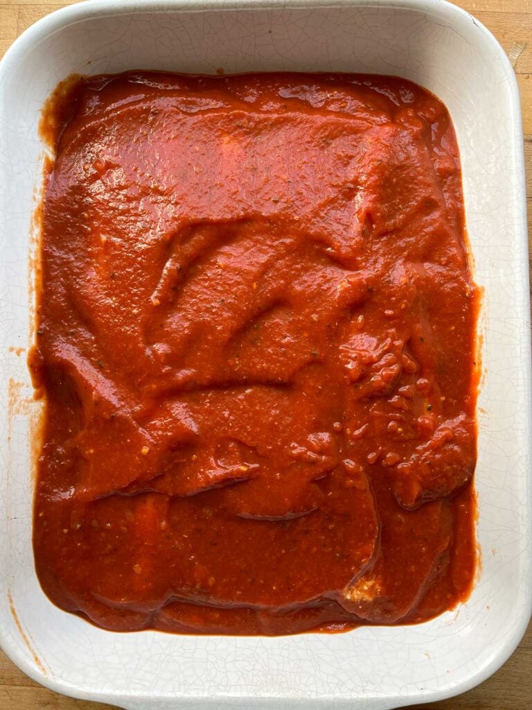 Cheese filled manicotti shells covered with marinara sauce before baking.